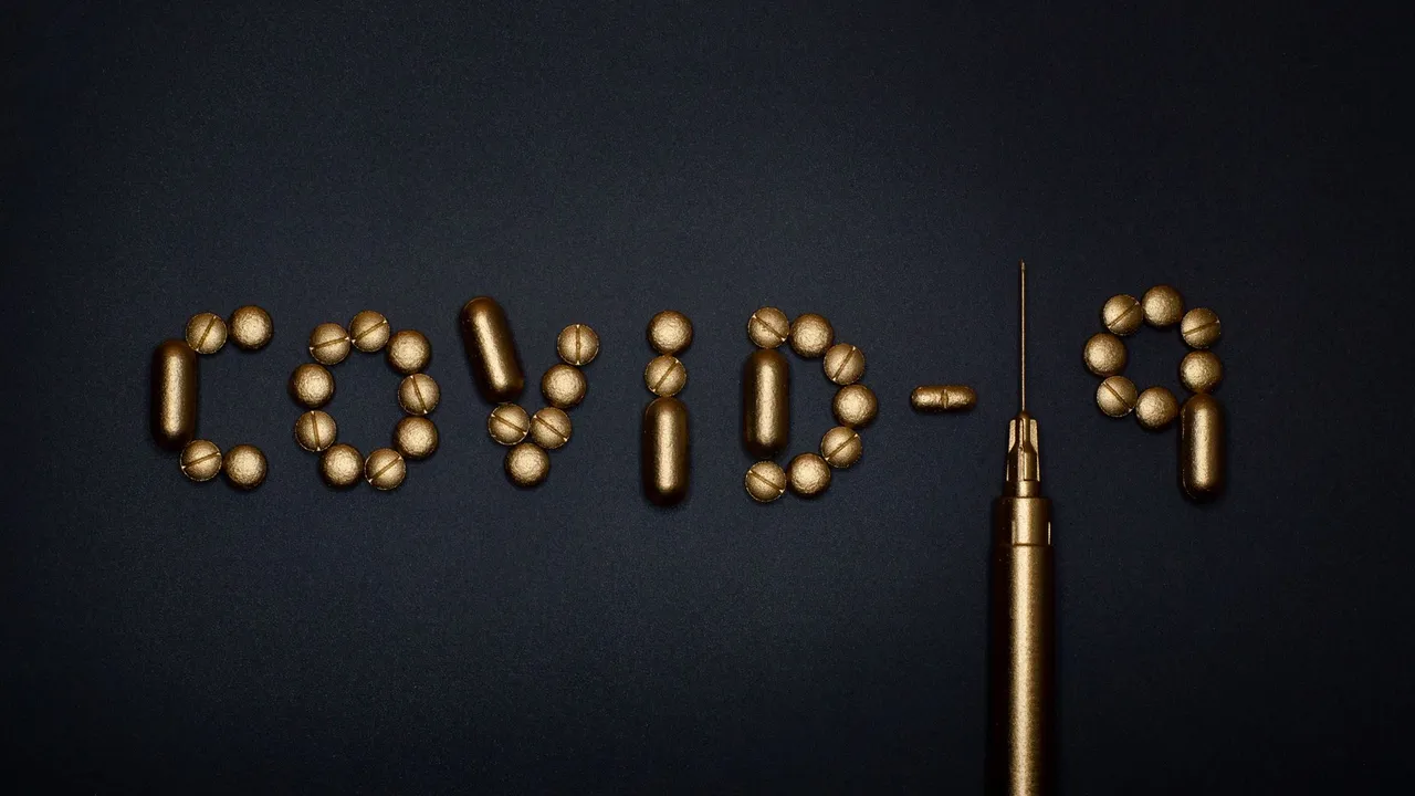 Artistic depiction of COVID-19 using pills and a syringe on a dark background, symbolizing medication.
