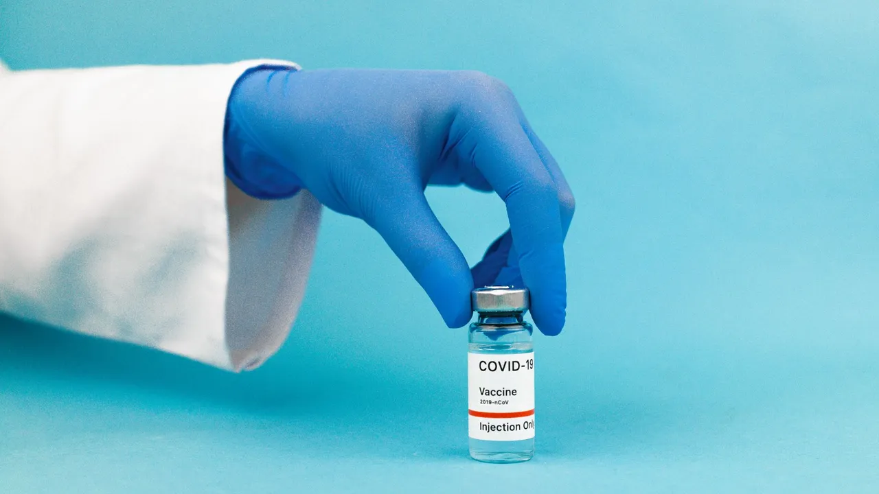 Medical professional hand wearing glove holding COVID-19 vaccine vial against blue background